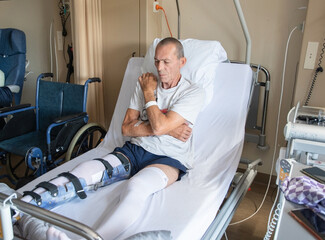 Obraz premium a man with a broken leg in an orthese in bed in a clinic after an accident,