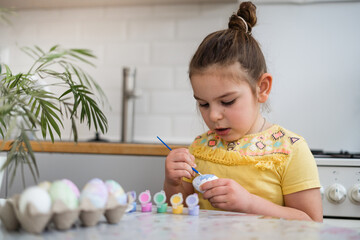 Child girl of preschool age painting Easter eggs at home kitchen. Easter spring traditions.
