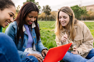 Young group of diverse college student studying together using laptop while having lunch at...