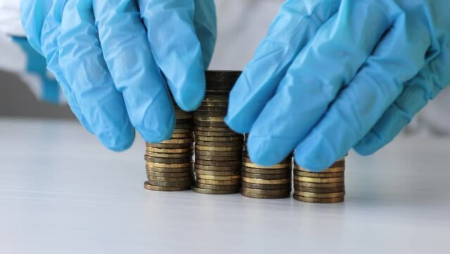 A doctor in protective gloves and a biological suit moves a tower of coins with both hands and it crumbles