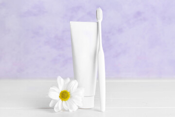 Tube of toothpaste, toothbrush and chamomile flower on light wooden table