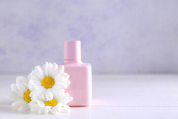 Fototapeta na wymiar Bottle of perfume and chamomile flowers on light wooden table