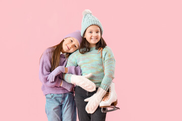 Little girls in winter clothes with ice skates hugging on pink background