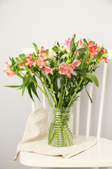Vase with beautiful alstroemeria flowers on chair near light wall, closeup