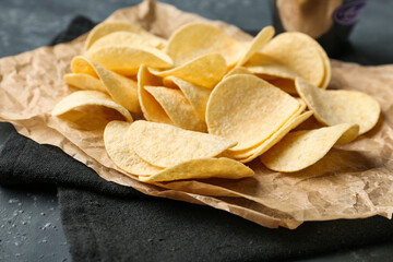 Parchment with delicious potato chips and bowl of ketchup on grey grunge background