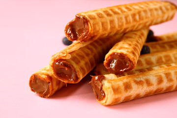 Delicious wafer rolls with boiled condensed milk and blueberries on pink background