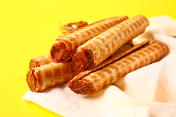 Delicious wafer rolls with boiled condensed milk on yellow background