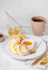 Plate with tasty cottage cheese pancakes, jam, honey and cup of tea on light background, closeup