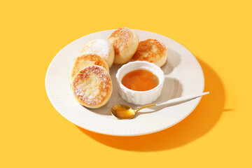 Plate with tasty cottage cheese pancakes and jam on yellow background