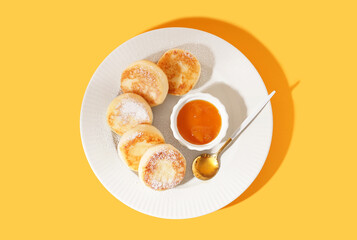Plate with tasty cottage cheese pancakes and jam on yellow background