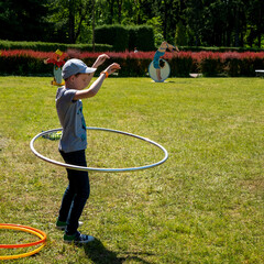 Young boy twirling hula hoop around his waist in the park. Exercise with the hoop. Summer activity