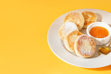 Plate with tasty cottage cheese pancakes and jam on yellow background
