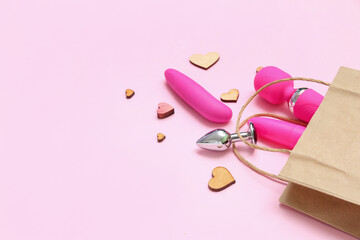 Shopping bag with sex toys and wooden hearts on pink background