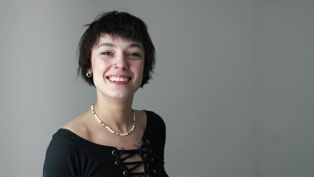 Stylish Gen Z optimistic woman looking at camera and smiling over grey background. Copy space. Importance of youth. High quality 4k footage