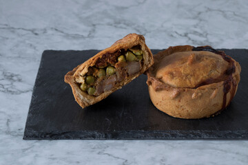Typical Mallorcan pastry product, the empanada. One whole and half of another on a slate tile and a marble countertop.