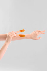Young woman applying sugaring paste onto arms against light background