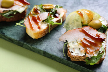 Board of tasty sandwiches with cream cheese, ham and sauce on color background, closeup