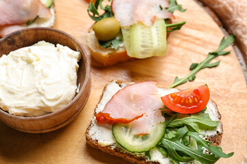 Wooden board with delicious sandwiches and cream cheese, closeup