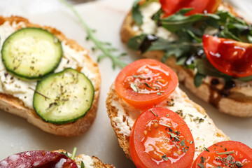 Tasty sandwiches with cream cheese, tomatoes and cucumber on board, closeup