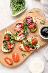 Wooden board with delicious sandwiches and sauce on light background, closeup