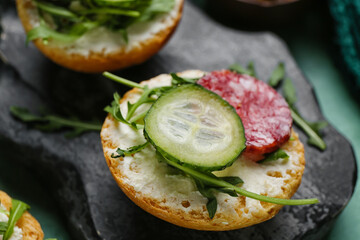 Tasty sandwich with cream cheese, salami and cucumber on board, closeup