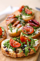 Wooden board of tasty sandwiches with cream cheese, arugula and tomatoes, closeup