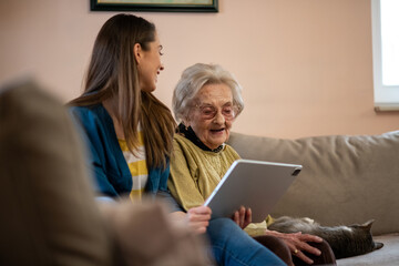 Senior woman and nurse discussing care options at a nursing home, using a tablet.