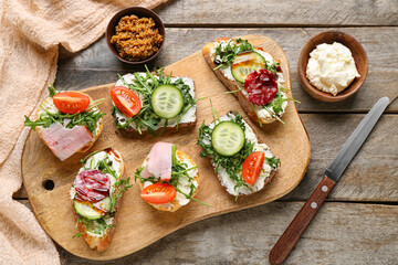 Board with tasty sandwiches, mustard and cream cheese on wooden background