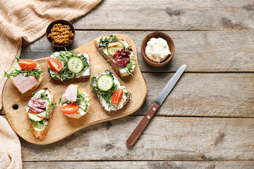 Board with tasty sandwiches, mustard and cream cheese on wooden background