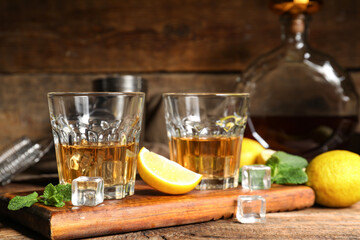 Board with glasses of rum, lime and ice cubes on wooden background