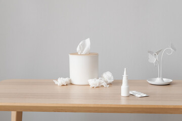 Fototapeta na wymiar Nasal drops with pills and tissue box on table near grey wall. Allergy concept