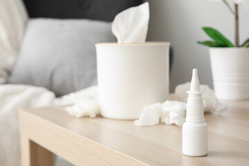 Fototapeta na wymiar Nasal drops with tissue box on table in living room, closeup. Allergy concept