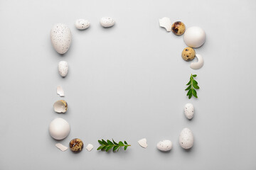 Frame made of Easter eggs and plant leaves on grey background