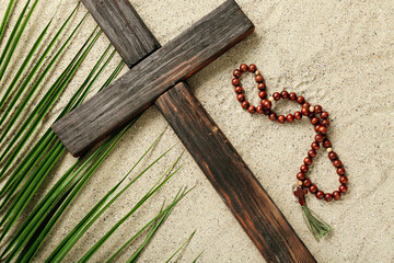 Wooden cross with prayer beads and palm leaf on sand. Good Friday concept