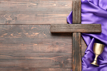 Cross with wine cup and purple fabric on wooden background. Good Friday concept