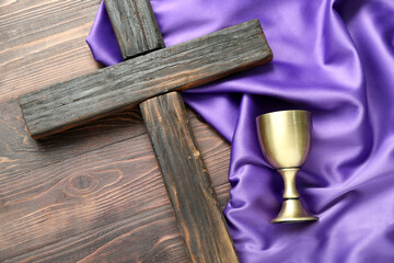 Cross with wine cup and purple fabric on wooden background. Good Friday concept
