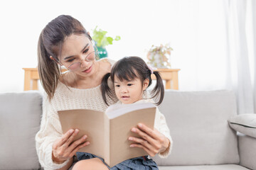 Asian children and her mother reading a book, they sitting on sofa, happiness in family time, child learning and development