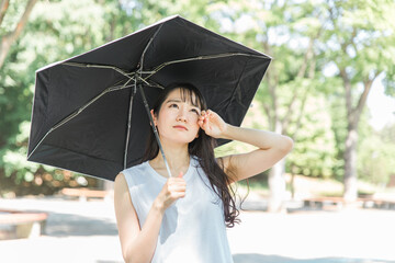 夏に熱中症対策・紫外線対策のため日傘をさすアジア人女性（疲労・汗）
