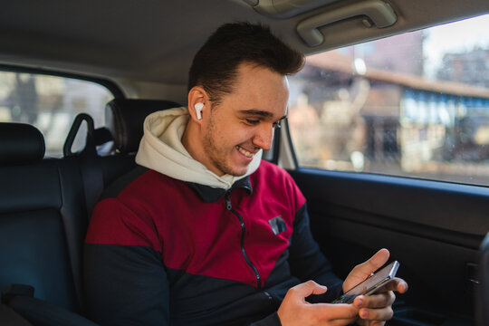 A Young Man Sitting In The Back Seat Of Car While Using His Phone And Waving Through The Window