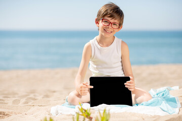 Boy sitting on the beach on a sunny day shows the empty screen of his tablet