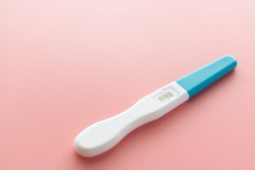 White Plastic Pregnancy test positive with two stripes results isolated on Pastel light pink background. Closeup.