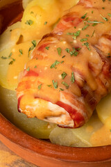 Chicken breast stuffed with cheese wrapped with strips of bacon in its sauce, over baked potatoes in a clay pot. Concept of rich and delicious cuisine.