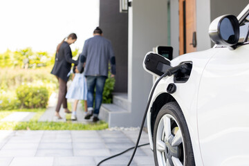 Focus closeup electric vehicle recharging battery from home electric charging station with blurred...