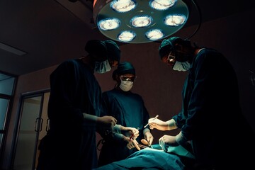 Surgical team performing surgery to patient in sterile operating room. In a surgery room lit by a...