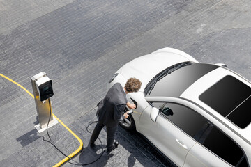 Aerial view of progressive businessman in black formal suit with his electric vehicle recharging...