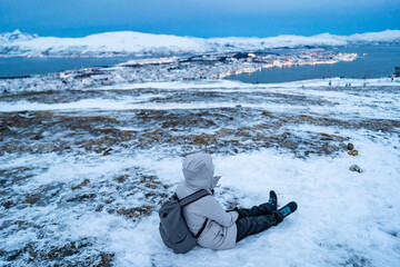 A tourist resting atop Fjellheisen overlooking the majestic fjords and city view of Tromso, Norway