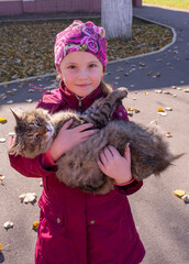  In autumn, a girl is holding a beautiful stray cat in her arms on the street.
