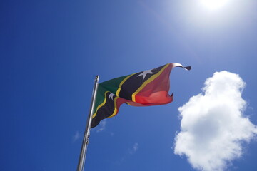 Saint Kitts flag waving in the sky with blue background and one white cloud