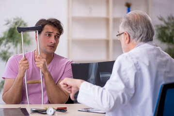 Fototapeta premium Young leg injured patient visiting old male doctor radiologist