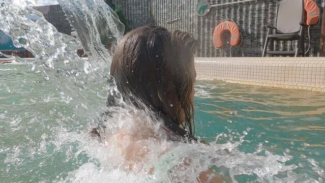 Relaxed woman in swimming pool enjoys bubble nack and shoulder hydromassage spa procedure from waterfall fountain. Body massage, relaxation, water treatment, hydrotherapy, aqua water park concept. 